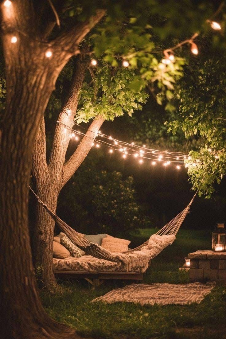 GetHovr garden hammock hanging between two trees in a British garden at night, fairy lights and lush greenery